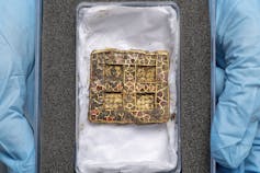 A square pendant in a cushioned box with crucifix detail and signs of previous life as a hinge on the sides.