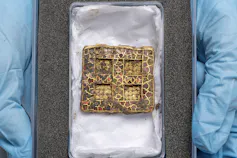 A square pendant in a cushioned box with crucifix detail and signs of previous life as a hinge on the sides.