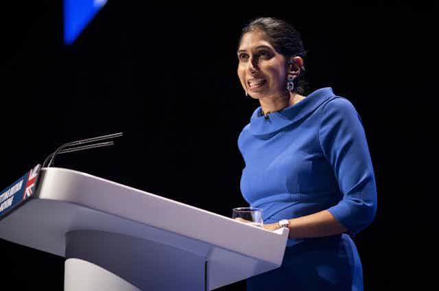 Suella Braverman in a blue dress speaks at a podium at the Conservative Party conference