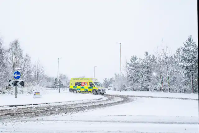 A yellow and green ambulance on a snowy road.