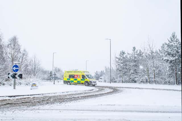 A yellow and green ambulance on a snowy road.