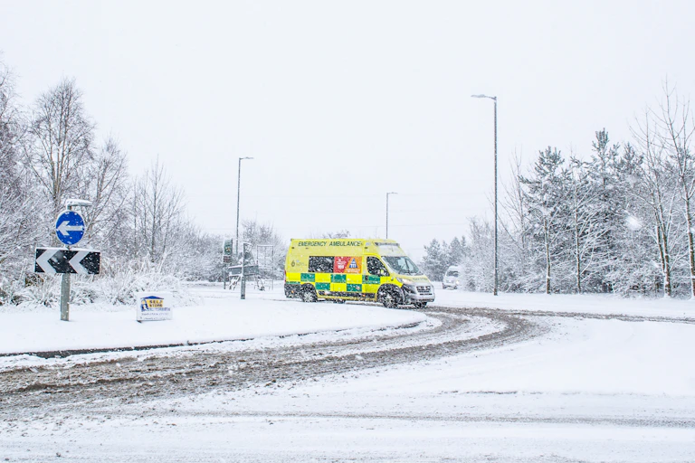 A yellow and green ambulance on a snowy road.