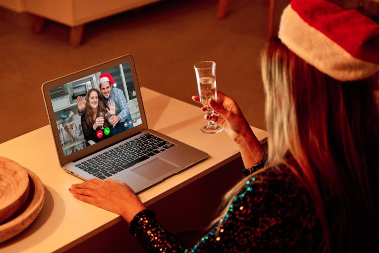 Woman with champagne looking at Zoom of family on laptop.