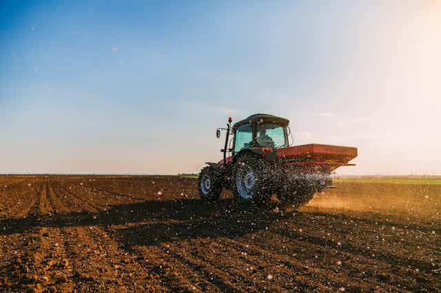 Tractor spreads fertiliser at sunset