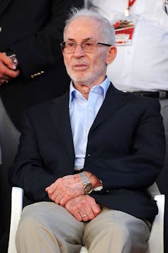 Photo of an elderly man in a black blazer and blue shift.