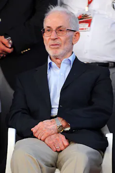 Photo of an elderly man in a black blazer and blue shift.