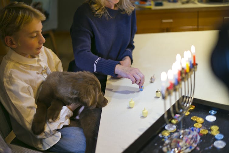 A boy holding a puppy sits with his family during the lighting of candles on a hanukkiah menorah.