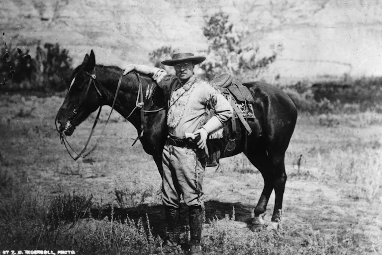A white man is standing on a field next to a horse