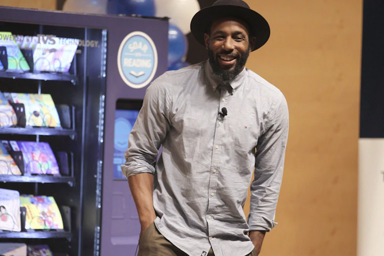 Stephen smiles in this photo. His hands are in his pocket; he wears a black hat.