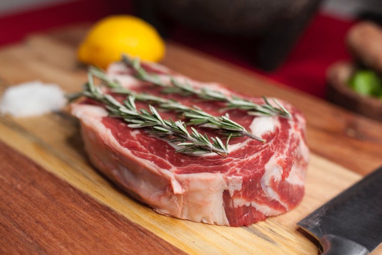 Cut of meat on chopping board with rosemary sprigs on top