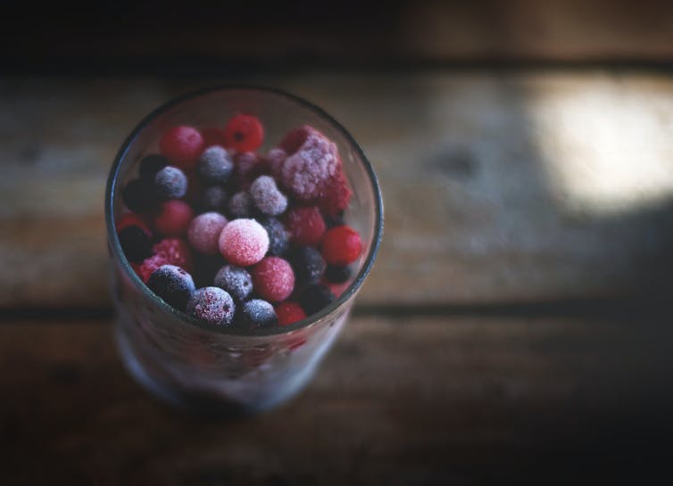 انواع توت های یخ زده در یک لیوان روی میز یا نیمکت چوبی
