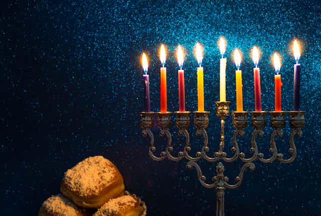 A candleholder with nine candles, shown against a sparkly blue background and baked goods.