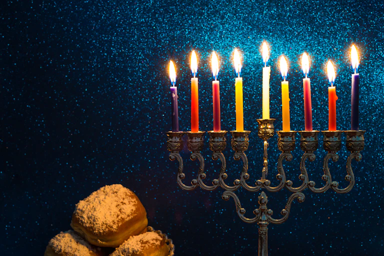 A candleholder with nine candles, shown against a sparkly blue background and baked goods.