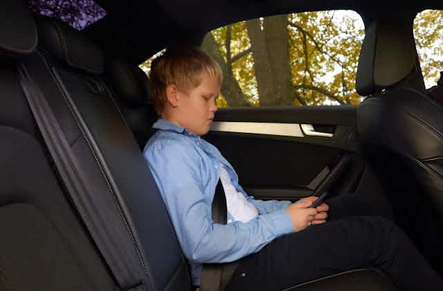 Boy looking at mobile phone as he rides alone in the back of a car