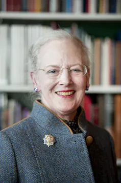 Queen Margrethe of Denmark in a royal portrait against a book shelf.