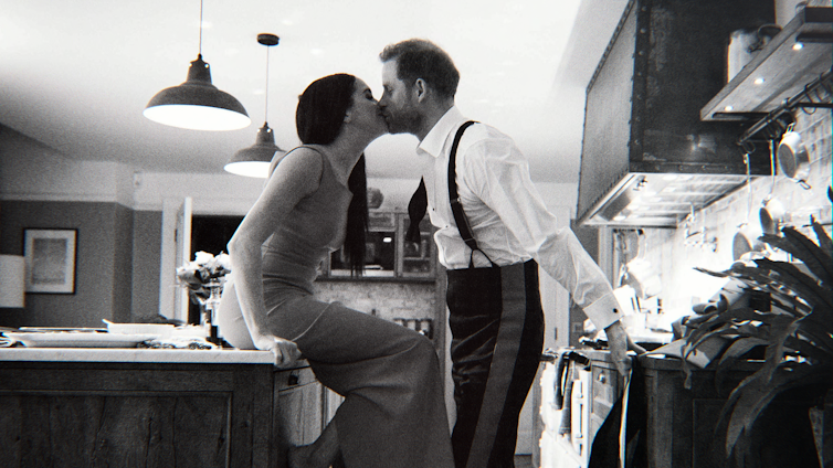 Harry en Meghan kussen elkaar in hun keuken op een zwart-witfoto die lijkt te zijn gemaakt met de zelfontspanner.