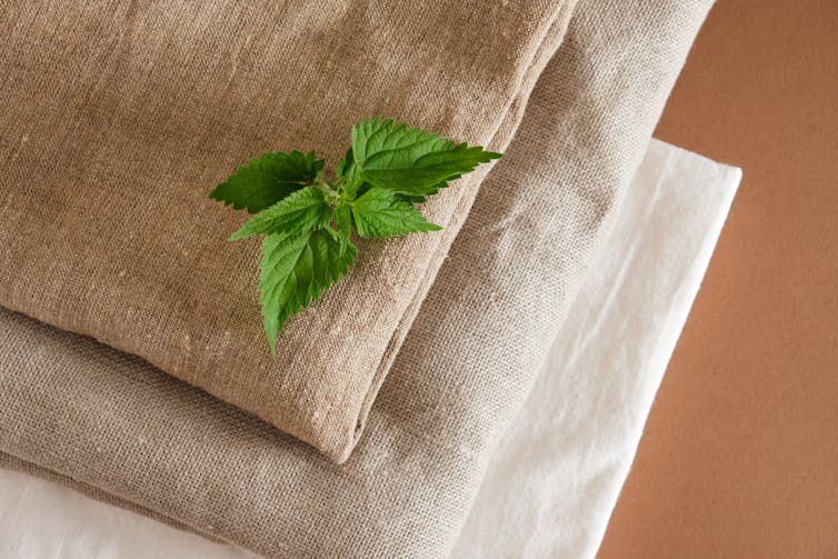 Nettle leaves and a stack of natural fabrics on a brown background