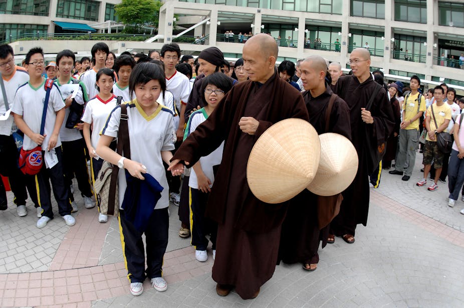 Buddhist monk in brown garb holding the hand of a young girl as other monks and children walk behind her.