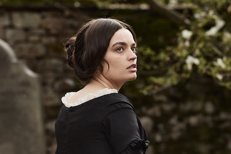 Wearing all black with her hair back, Emily looks off into the distance.