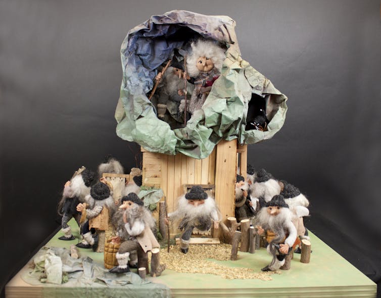 A diorama made of felt and wood shows elves with beards gathered around a taller structure with more elves inside.