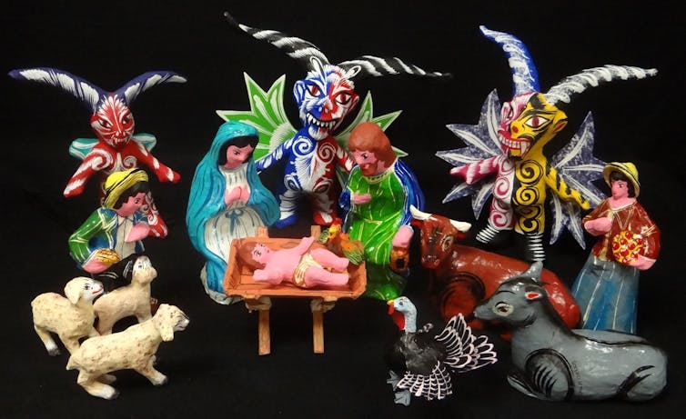 A Nativity set in bright colors, with three devilish figures standing behind the Holy Family.