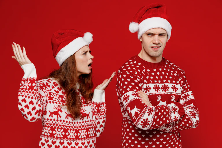 A young man and woman in red Christmas jumpers and santa hats, arguing with each other