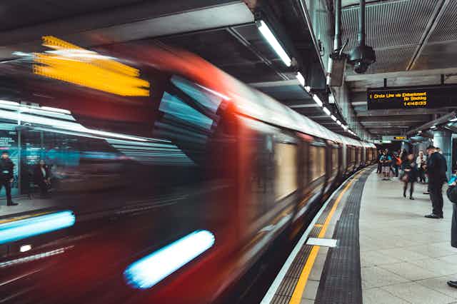 A train driving past a busy London Underground platform.