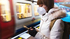 A woman seated and scrolling through her phone while a train moves past in the background.