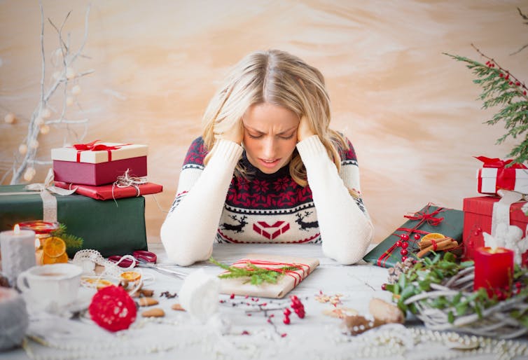 A woman sitting with her head in her hands at a table covered in Christmas presents and decoration