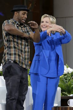 TWitch dances with Hillary Clinton in a blue suit.