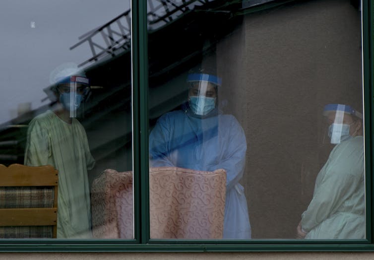 Three people in PPE seen through a window