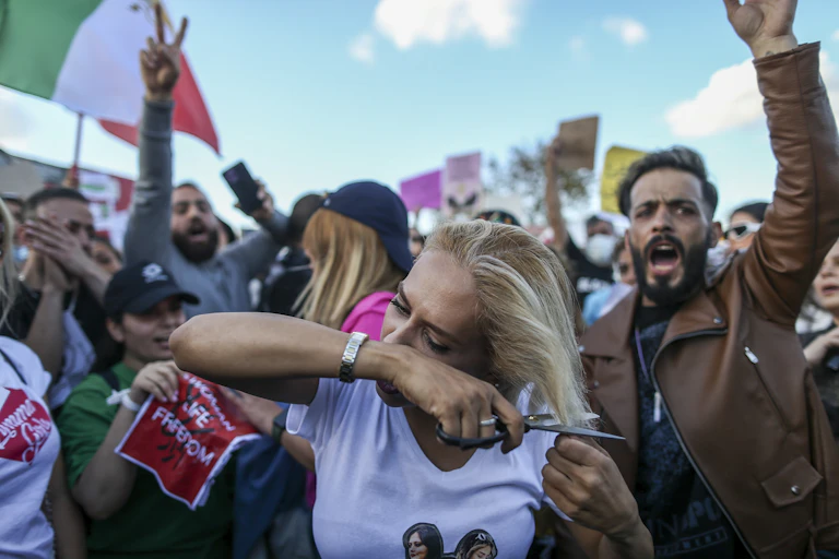 A woman with blond hair cuts part of it with scissors during a protest march.