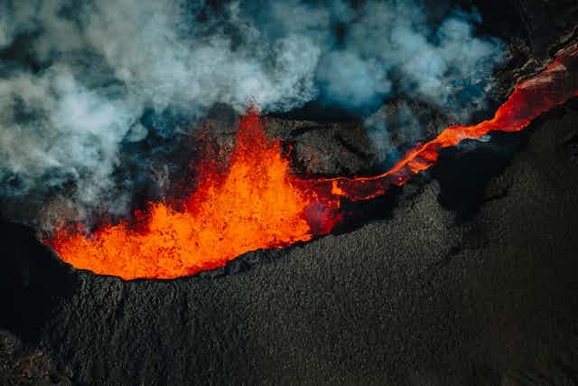 With clouds of smoke and ash billowing above, bright orange magma spews out of the volcano's top. 