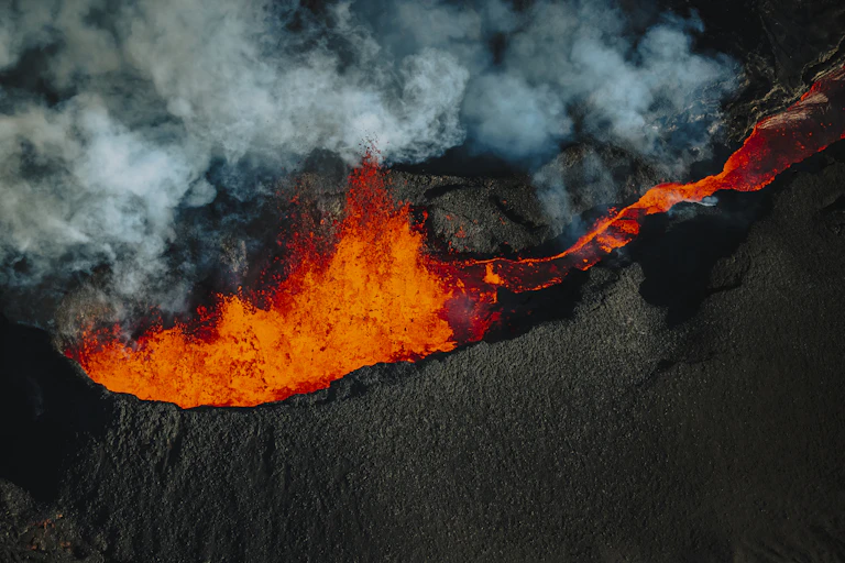 With clouds of smoke and ash billowing above, bright orange magma spews out of the volcano's top.