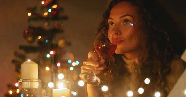 A curly-haired woman drinking alone near a Christmas tree, candles and lights