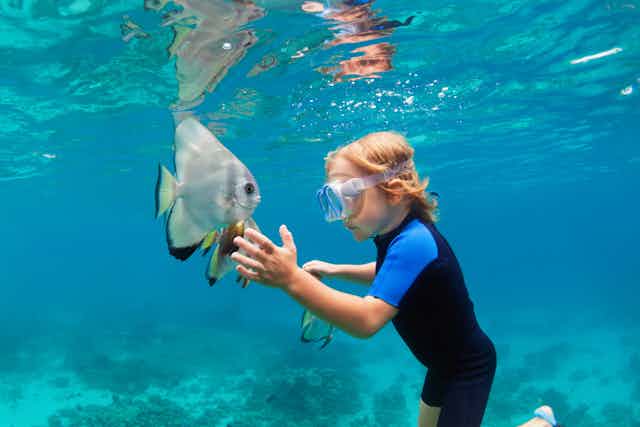 boy reaches out to fish underwater 