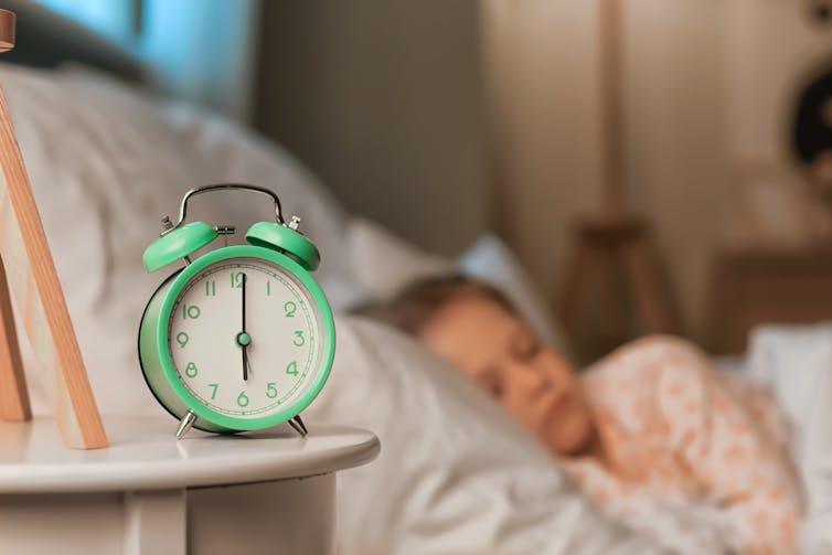 Girl sleeps with clock in foreground