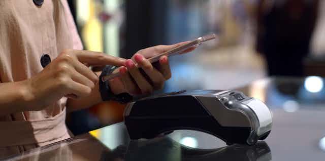 Woman using phone near store's EFTPOS terminal..
