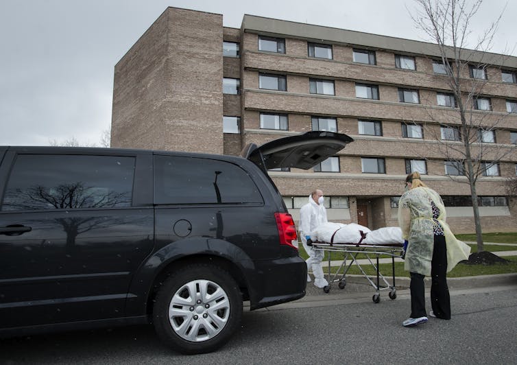 A person wearing PPE beside a gurney behind a van.