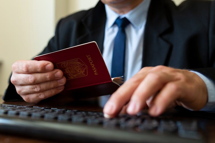 close up on hands of immigration officer holding a passport and typing on a keyboard to check details