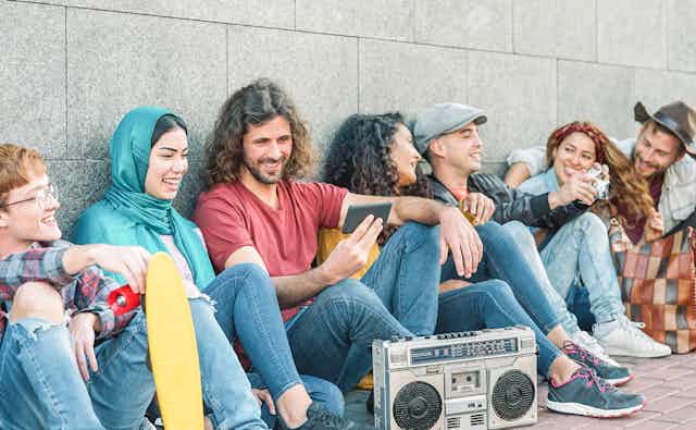 A group of hip millennial friends smile as they listen to music from a phone.