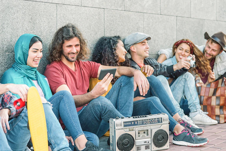 A group of hip millennial friends smile as they listen to music from a phone.