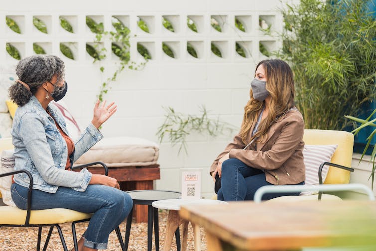 two women in masks sit outside talking