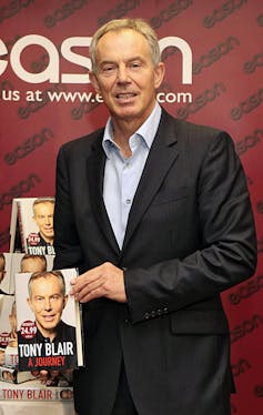 Tony Blair smiles holding a copy of his memoir, A Journey