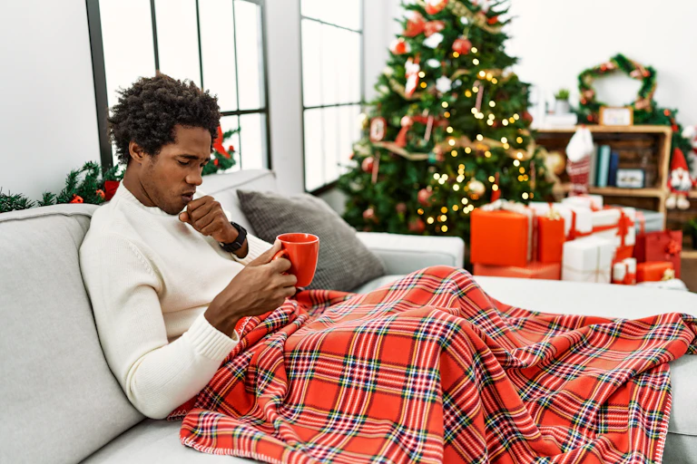 A man appears unwell, with a Christmas tree in the background.