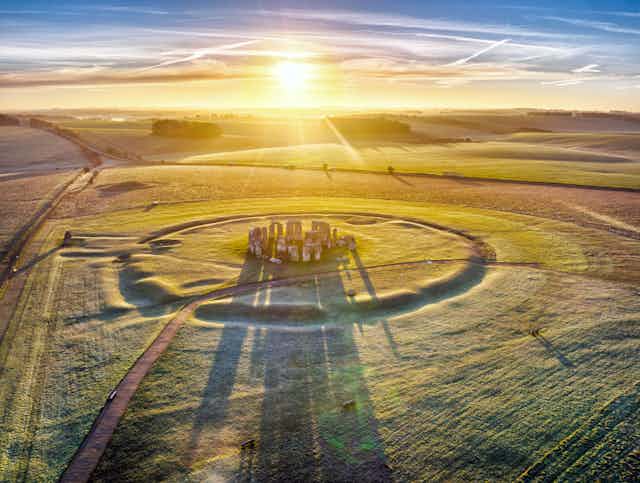 The sun shines over a vast field dusted with snow, with Stonehenge in the middle.