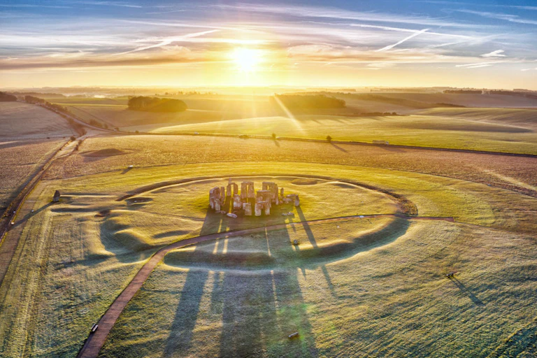 The sun shines over a vast field dusted with snow, with Stonehenge in the middle.