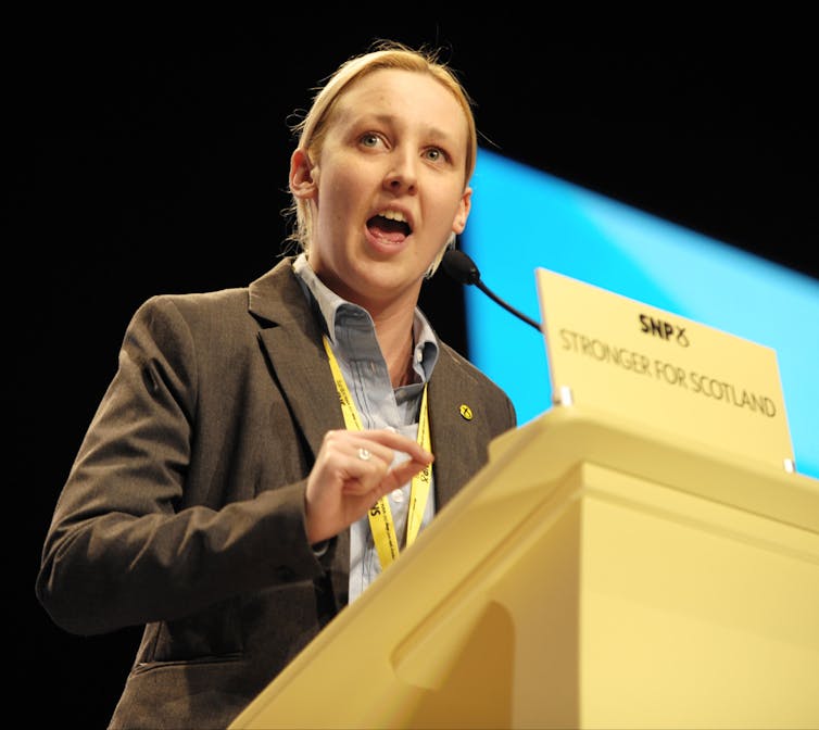 Mhairi Black, wearing a suit, speaks at a podium behind a placard reading Stronger for Scotland.