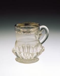 A clear miniature glass ale jug with silver rim.