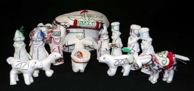 A Nativity set with all white animals and figures, decorated with colored stitching.